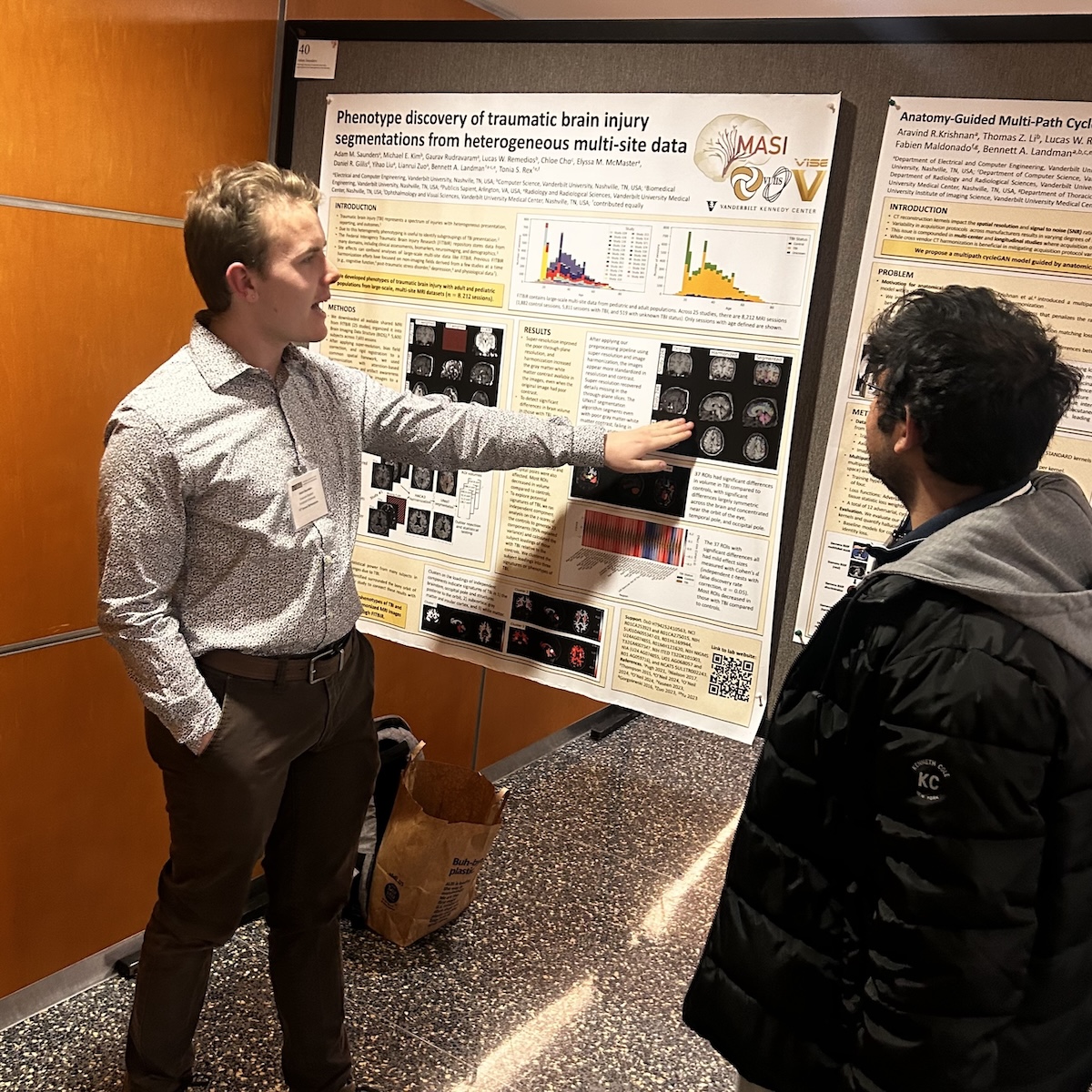 A picture of me and a labmate standing in front of a poster titled 'Phenotype discovery of traumatic brain injury segmentations from heterogeneous multi-site data'.
